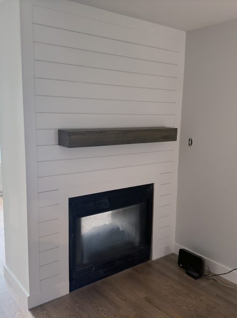 Interior of a home with a large bright window and hardwood floors. A newly renovated fireplace is the focal point of the room.